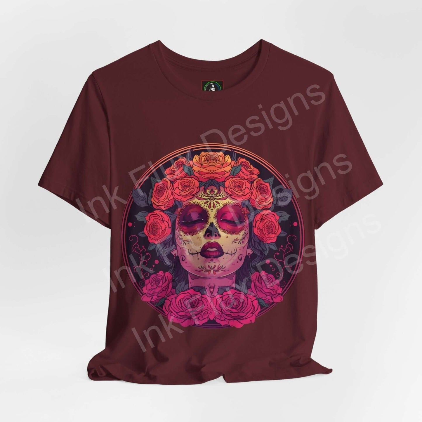 Day of the Dead themed graphic tee featuring a vibrant DÃa de Muertos skull adorned with floral designs on a burgundy T-shirt.