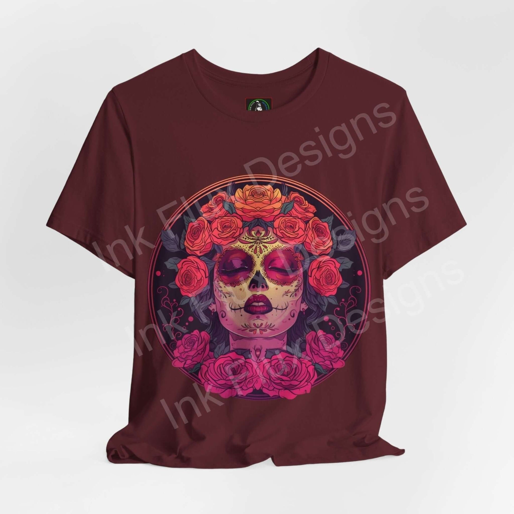 Day of the Dead themed graphic tee featuring a vibrant DÃa de Muertos skull adorned with floral designs on a burgundy T-shirt.