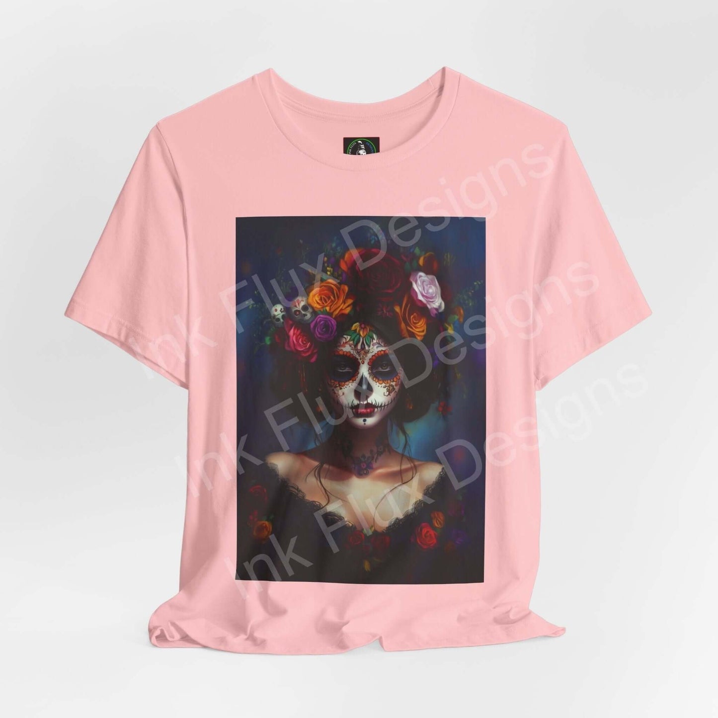 Pink T-shirt featuring a Day of the Dead themed graphic with a woman's portrait adorned in colorful floral elements, by Bella+Canvas.