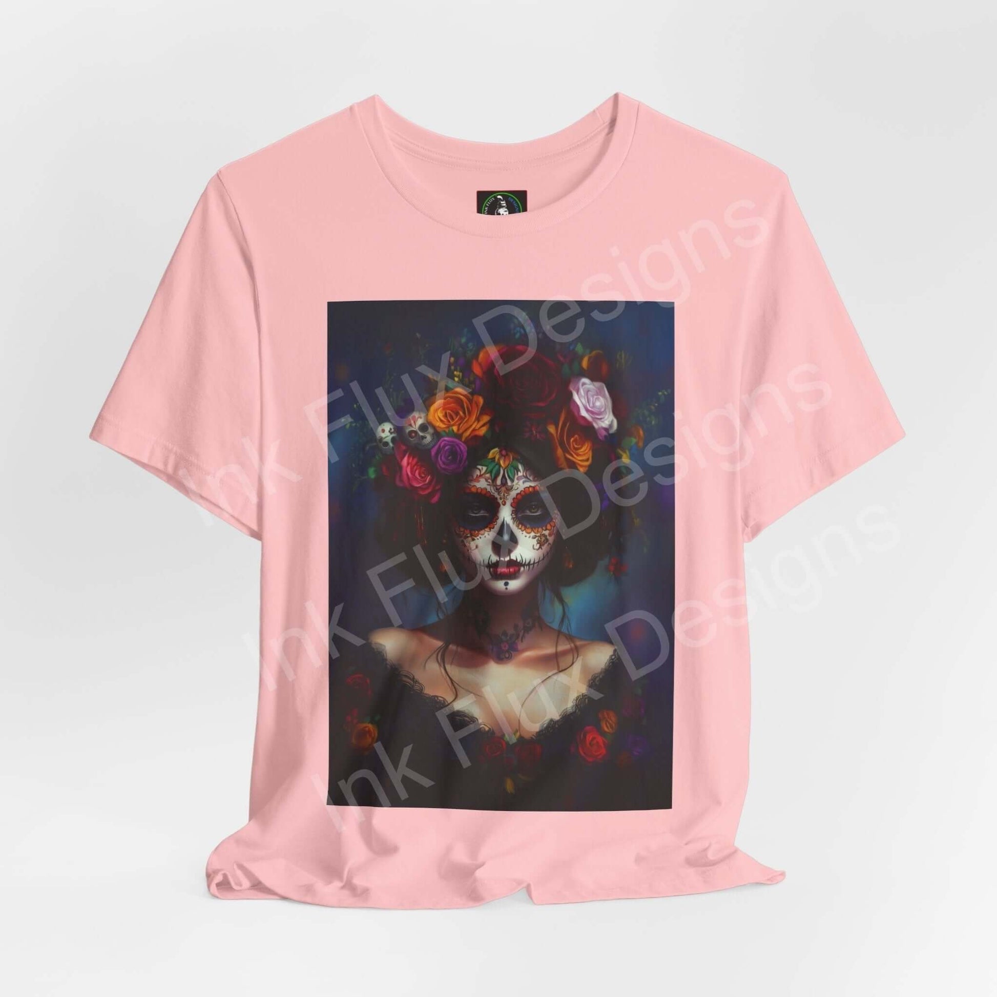 Pink T-shirt featuring a Day of the Dead themed graphic with a woman's portrait adorned in colorful floral elements, by Bella+Canvas.