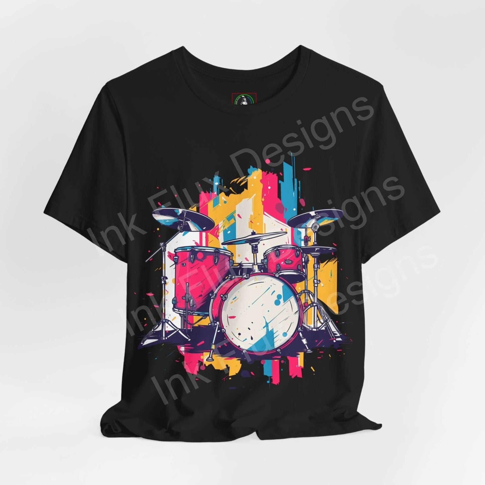 Black unisex T-shirt featuring a bold, colorful graphic of a drum set in pink, blue, and yellow splashes on Bella+Canvas jersey fabric.