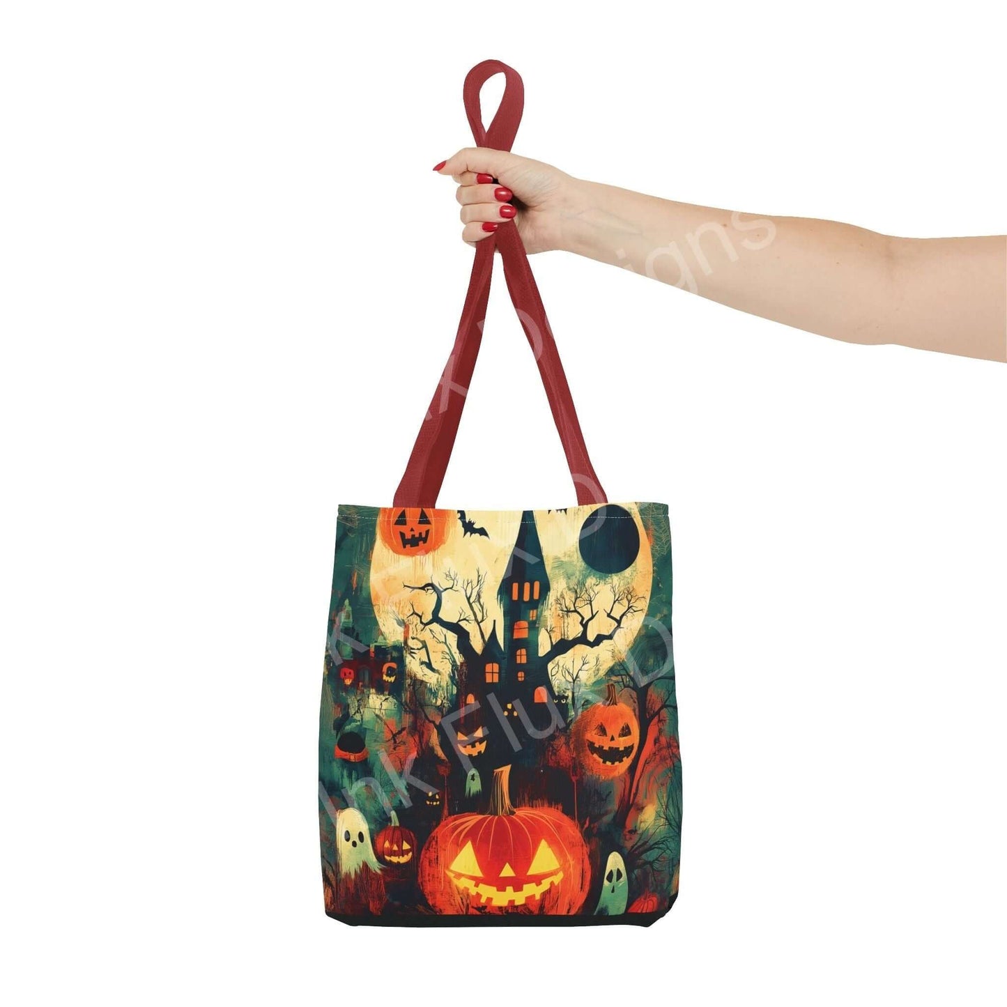 Hand holding a Halloween-themed tote bag featuring a haunted house and pumpkins design, with red straps, perfect for festive occasions.