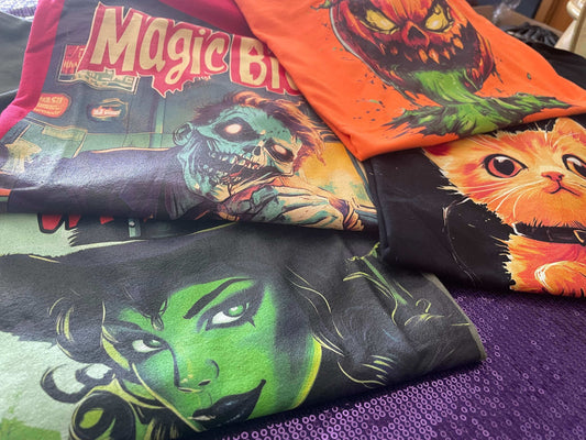 Assortment of Halloween themed t-shirts featuring spooky characters and vivid colors displayed on a purple background.