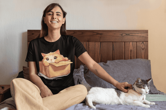 Woman sitting on bed wearing cat design t-shirt, smiling, petting a white and grey cat.