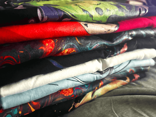 Fresh Ink on Fabric — New Samples Just Landed: Stack of vibrant T-shirts showcasing bold graphics and colors.